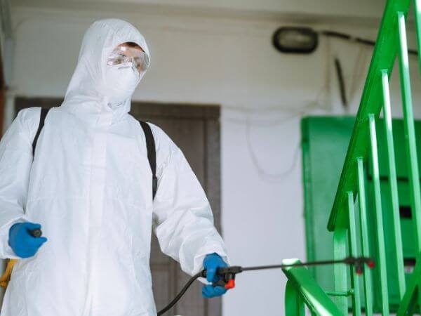 operatore con tuta bianca all'interno di una struttura per la disinfestazione